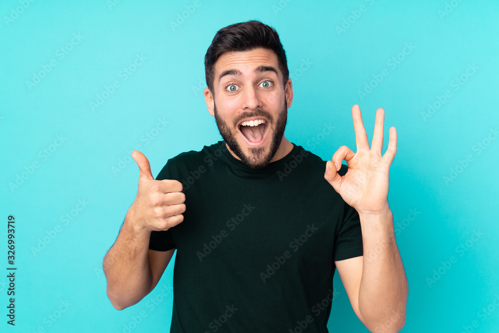 Caucasian handsome man isolated on blue background showing ok sign and thumb up gesture Caucasian handsome man isolated on blue background showing ok sign and thumb up gesture