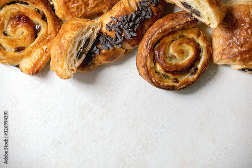 Variety of traditional french puff pastry buns with rasin and chocolate, croissant over white texture background. Flat lay, space photo