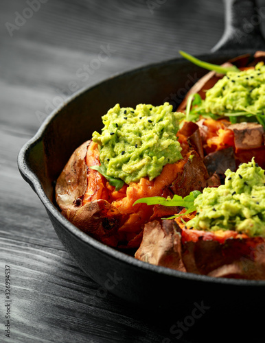 Baked Sweet potato boats stuffed with avocado guacamole and wild rocket sprinkled with nigella seeds in cast iron pan