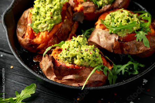 Baked Sweet potato boats stuffed with avocado guacamole and wild rocket sprinkled with nigella seeds in cast iron pan