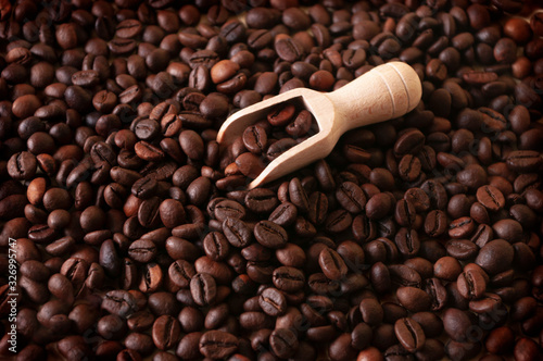 roasted coffee on wooden scoop, brown beans background
