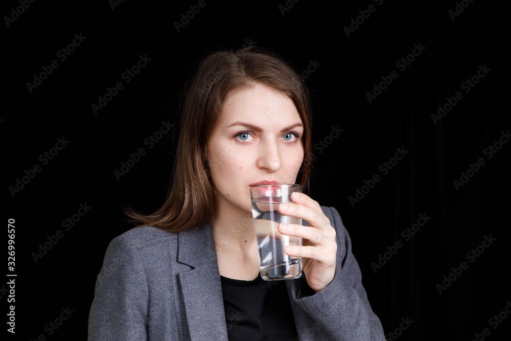 Portrait of a woman drinking water and looking into the camera. Portrait on a black background Portrait of a woman drinking water and looking into the camera. Portrait on a black background