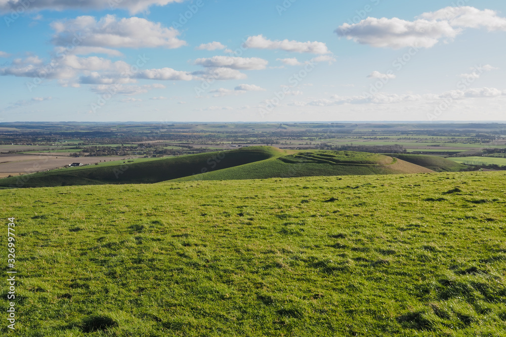 View from top of Tan Hill, the second highest point in Wiltshire, overlooking Cliffords Hill, the Vale of Pewsey and Salisbury Plain, with blue sky and white clouds, North Wessex Downs, UK