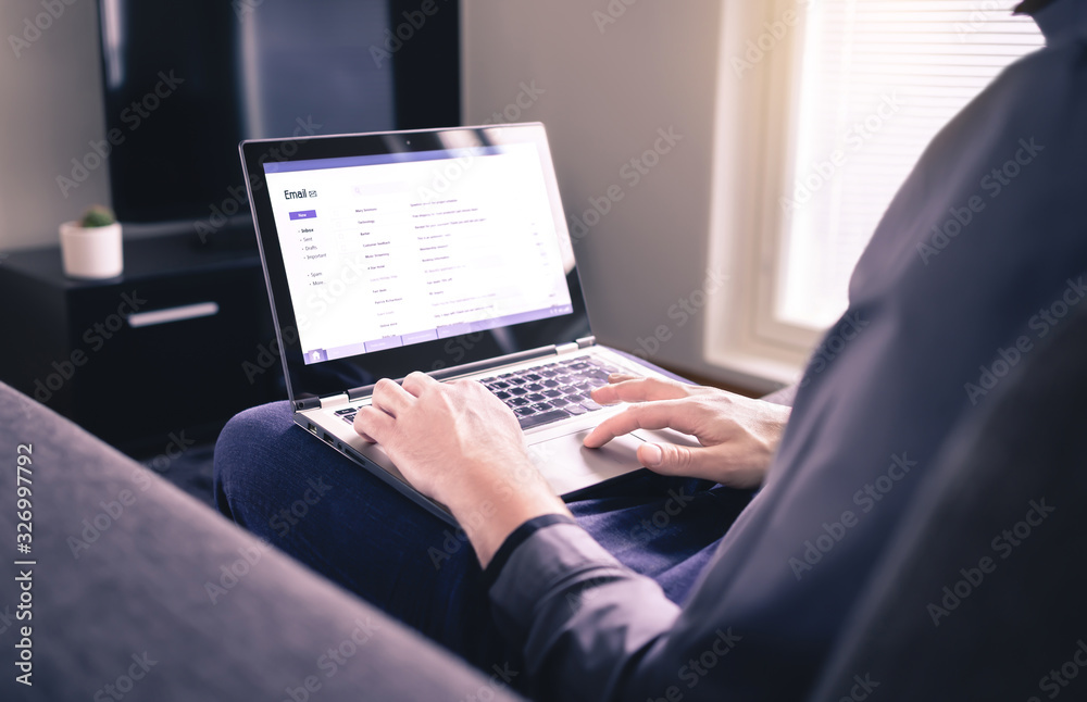 Man reading email and using laptop in home living room. Checking received electronic web mail and replying to messages. Mockup inbox on computer screen. Business lifestyle and entrepreneurship. Man reading email and using laptop in home living room. Checking received electronic web mail and replying to messages. Mockup inbox on computer screen. Business lifestyle and entrepreneurship.