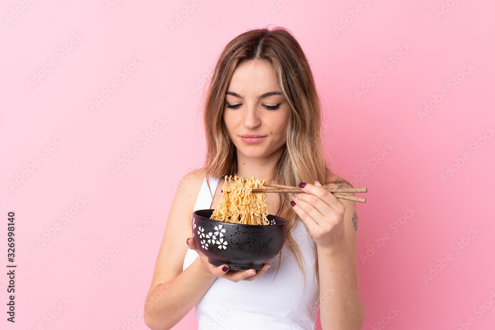 Young woman over isolated pink background holding a bowl of noodles with chopsticks Young woman over isolated pink background holding a bowl of noodles with chopsticks