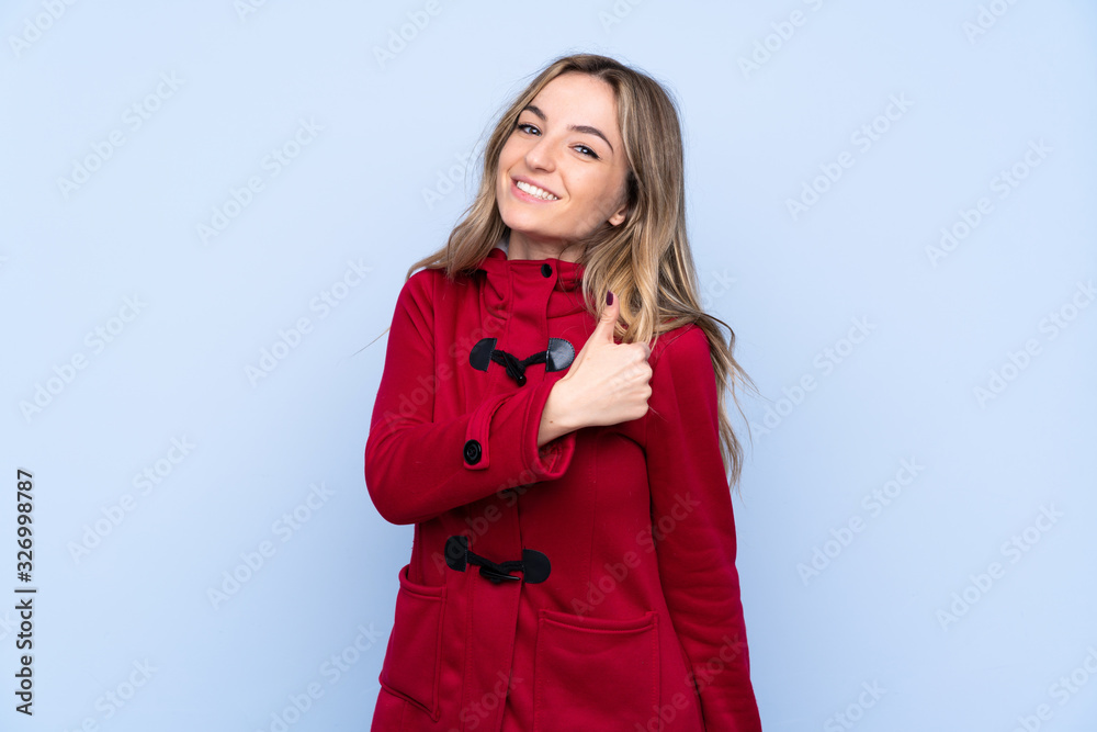 Young woman with winter coat over isolated blue background giving a thumbs up gesture Young woman with winter coat over isolated blue background giving a thumbs up gesture