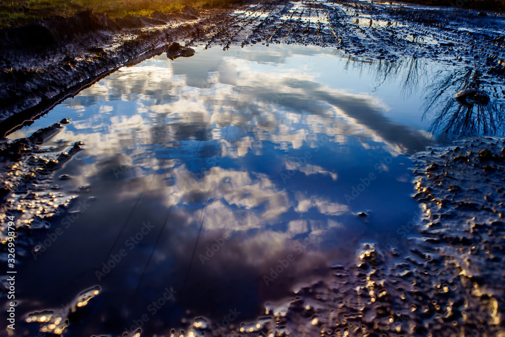 HDR photo of the setting sun reflecting in a puddle. View of the side road and trees. HDR photo of the setting sun reflecting in a puddle. View of the side road and trees.