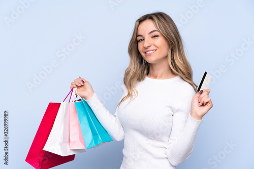 Young woman over isolated blue background holding shopping bags and a credit card