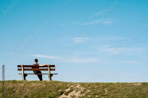 Fototapeta lonely man siting on a bench on an empty landscape