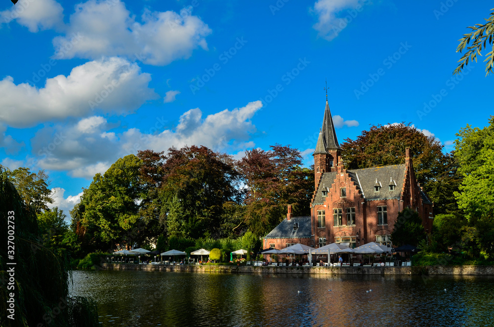 Bruges, Belgium. August 2019. The lake and minnewater park are the most romantic place. The body of water on which the red brick castle and the large trees with green foliage are reflected.