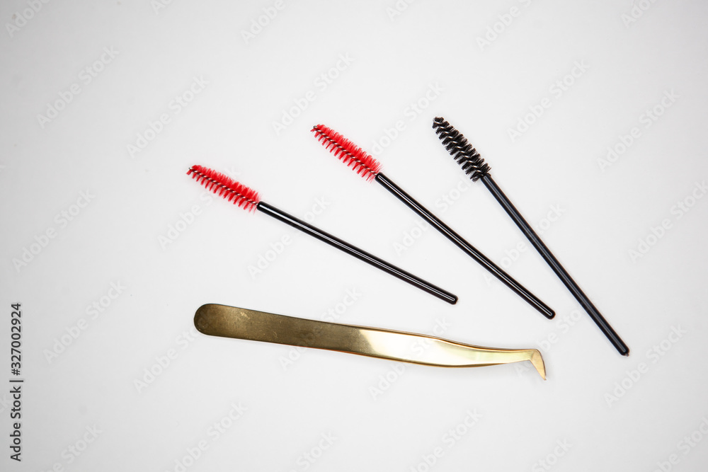 eyelash extension tools, golden tweezers and red-black brushes on a white background eyelash extension tools, golden tweezers and red-black brushes on a white background