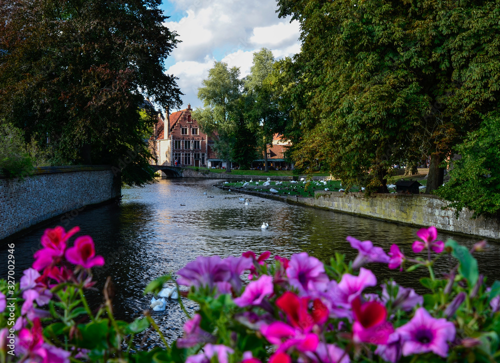 Bruges, Belgium. August 2019. View towards the historic center from the bridge with the Sashuis lock. A planter frames the canal that leads the gaze towards the city. Large green foliage on the sides.