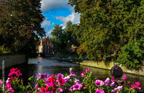 Bruges, Belgium. August 2019. View towards the historic center from the bridge with the Sashuis lock. A planter frames the canal that leads the gaze towards the city. Large green foliage on the sides.