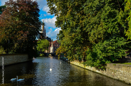 Bruges, Belgium. August 2019. View towards the historic center from the bridge with the Sashuis lock. The canal leads the eye towards the city. Large green foliage on the sides.