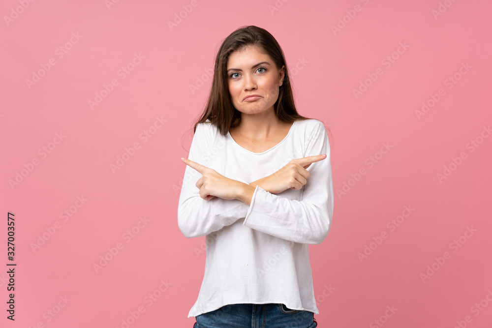 Young woman over isolated pink background pointing to the laterals having doubts Young woman over isolated pink background pointing to the laterals having doubts