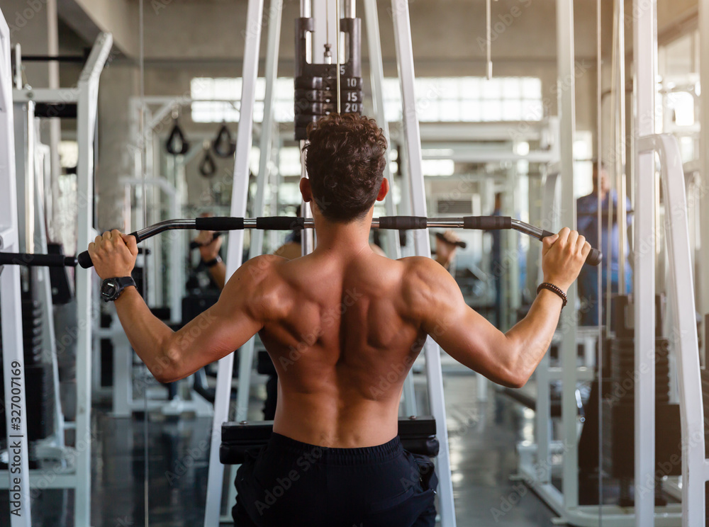Back view man doing workout exercise with thrust of the upper block in the gym Back view man doing workout exercise with thrust of the upper block in the gym