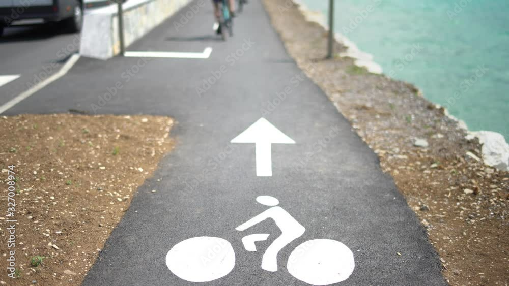 Bicycle path with a white sign of a bike on the street. Cyclists commuters or tourists riding bikes on the cycle lane in ta coastal city near the ocean or the sea. Cine lens.