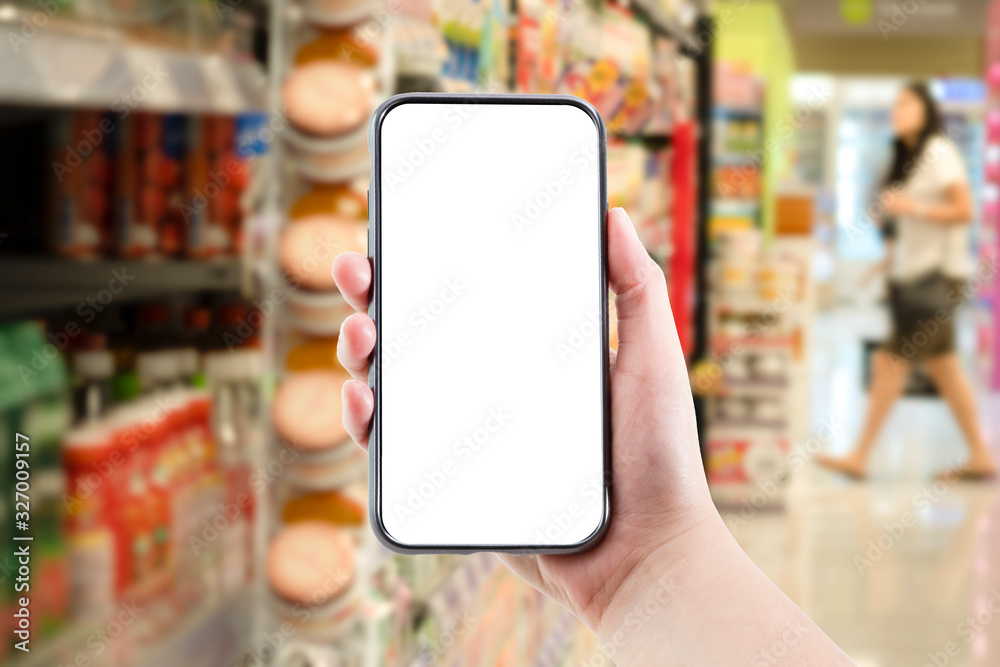 Hand holding blank form of mobile phone with supermarket or shopping mall background. Online shopping or e commerce concept. Hand holding blank form of mobile phone with supermarket or shopping mall background. Online shopping or e commerce concept.