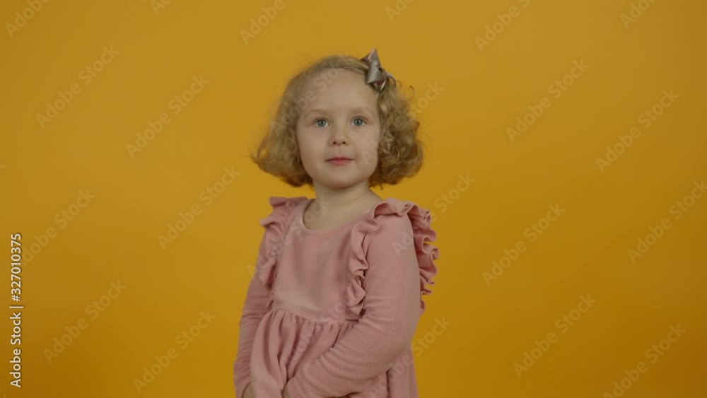 Cute curly kid in dress looking around on yellow background Cute curly kid in dress looking around on yellow background