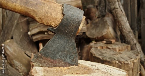 A metal ax is stuck in a log. Brown firewood lies in the background, they are a source of heat and energy in village houses.