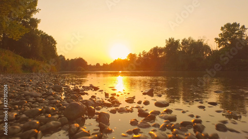 AERIAL, CLOSE UP: Rocky riverbank and water surface reflecting golden sky