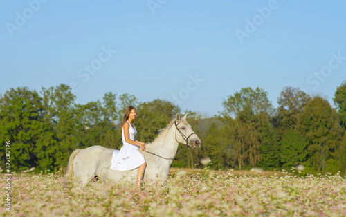 Girl in white dress bareback riding white horse in blooming field