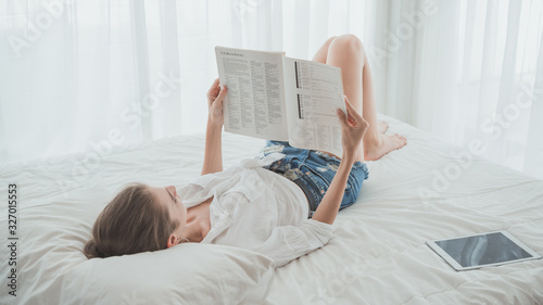 Young beautiful caucasian woman reading on the book while laying down on the bed