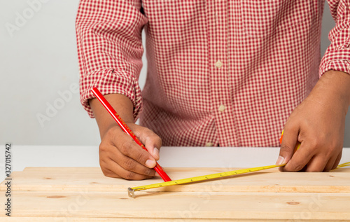 joiner measuring a wooden plank with tape measure yellow on the work-table for construction, photo