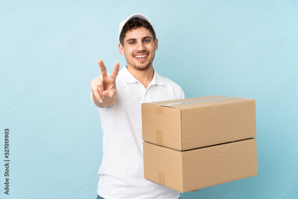 Delivery caucasian man isolated on blue background smiling and showing victory sign Delivery caucasian man isolated on blue background smiling and showing victory sign