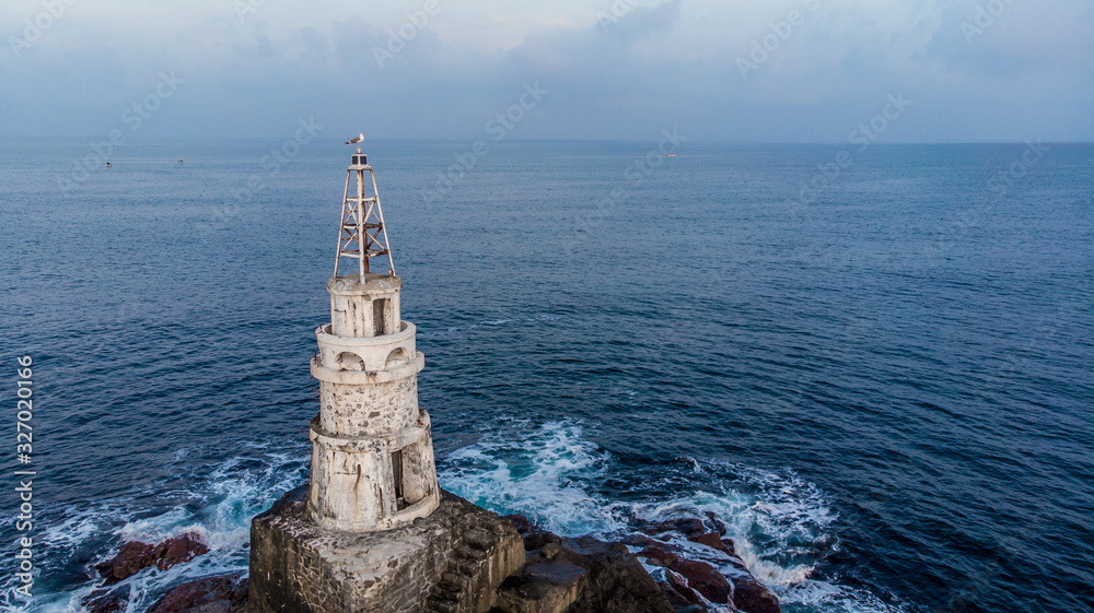 Lighthouse with a seagull on top, over the blue sea