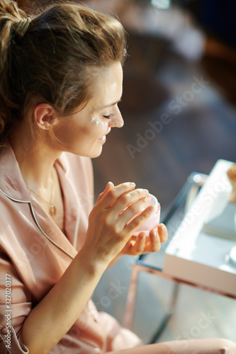 happy modern female with pink cosmetic jar applying eye cream