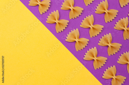 Raw pasta farfalle on purple background with copyspace. Poster.