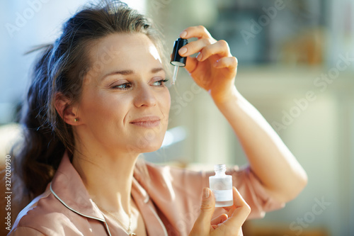 woman in modern house in sunny winter day using cosmetic elixir photo