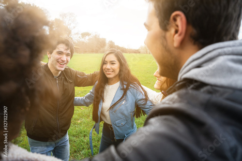 Group of teenagers of different cultures hugging each other at the park - Teamwork of young people forming a semicircle - Six men and women having fun together