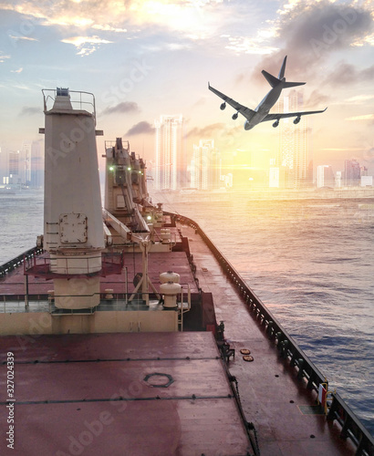 General cargo ship argosy cruising on ocean with plane to urban city at sunrise