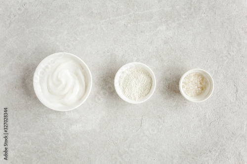 Female skin and body care cosmetic products set: facial cream, cosmetic clay, sea salt on gray marble background. Beauty blogger, salon treatments concept. Flat lay, top view
