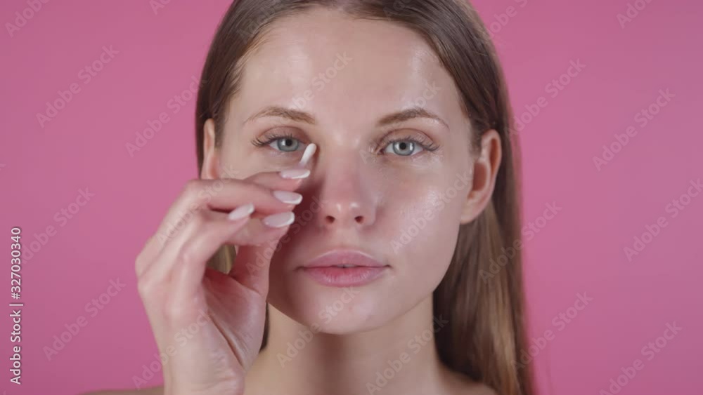 Portrait of beautiful young woman standing against pink background and using cotton swab under her eye Portrait of beautiful young woman standing against pink background and using cotton swab under her eye