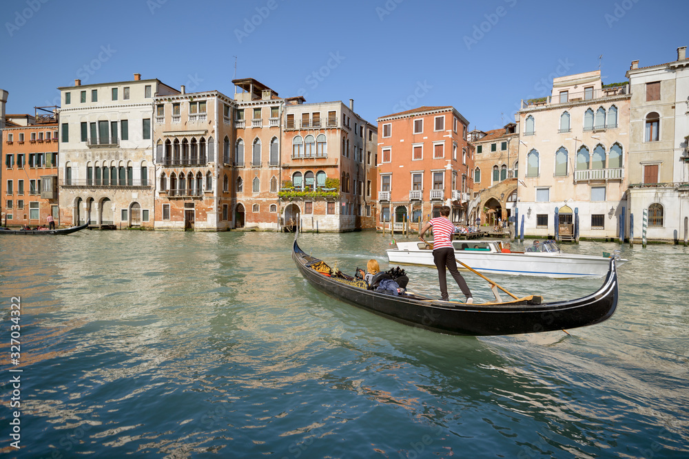 Gondolier in dance pose with a passenger in his gondola, crossing water taxi in Grand Canal, Venice, Italy