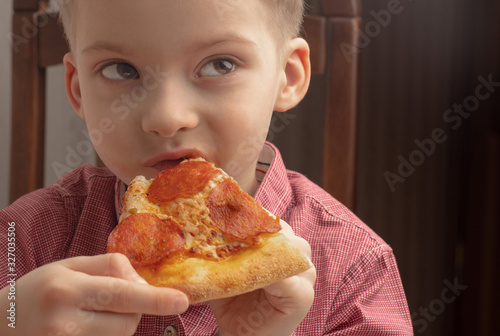 little boy eats a slice of pepperoni pizza. kids love pizza