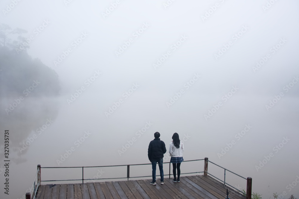 A lover is standing on a lakeside in a foggy day