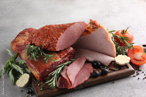 Assorted meat. Beef, pork, carbonate with garlic, olive, spices, herbs, rosemary and tomatoes on a wooden board. Light background. Background image, copy space
