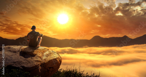 a man sitting on the big rock on a cliff and enjoying the foggy morning sunrise in mountains.