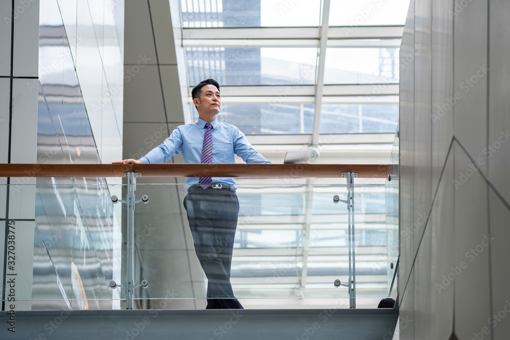 Thoughtful businessman looking away in the lobby of a bright modern business building stock photo. Businessman looking away, thinking of new ideas, planning project or waiting for somebody to come Thoughtful businessman looking away in the lobby of a bright modern business building stock photo. Businessman looking away, thinking of new ideas, planning project or waiting for somebody to come