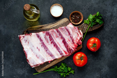 raw pork ribs with spices  tomatoes and herbs on a stone background