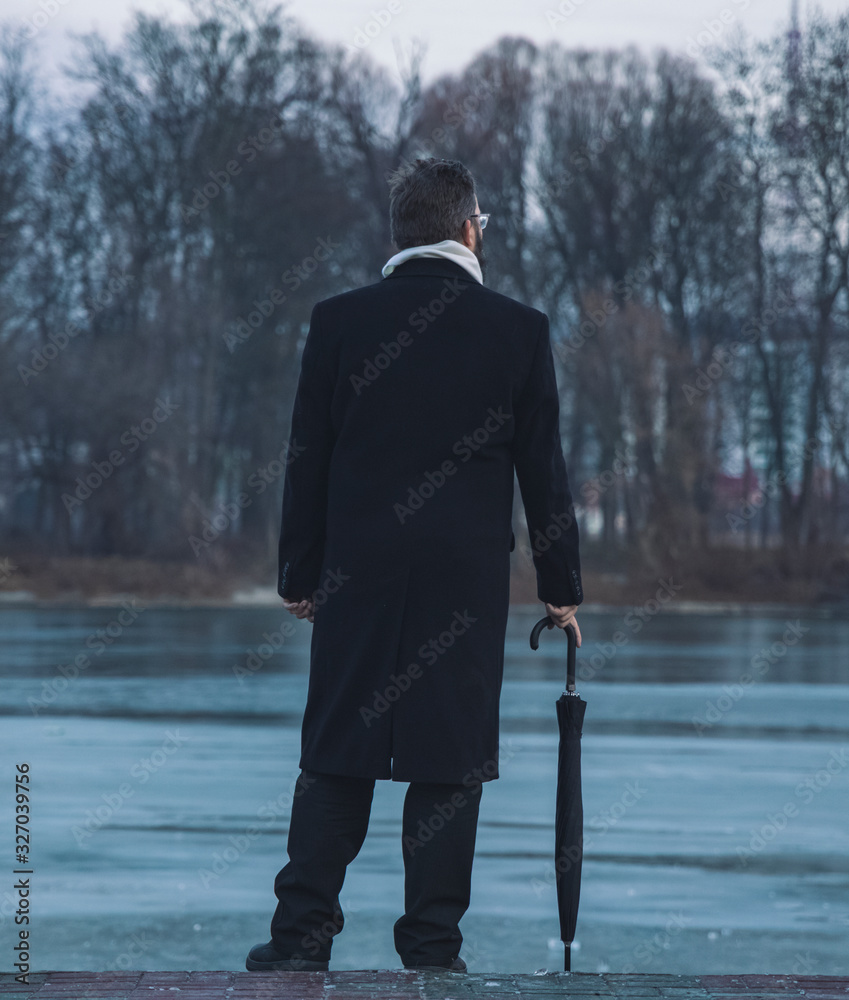 soft focus depressive photography concept of one adult man in black coat stay back to camera on waterfront edge near lake reservoir outdoor background space vertical