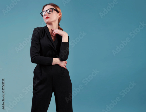 elegant business woman in black classic overalls and glasess posing over blue background. Happy satisfied relaxed elegant woman enjoy her work photo