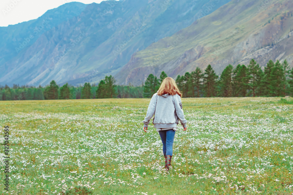 the girl stands with her back against the mountains