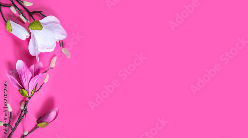 A branch of an artificial orchid flower on a pink background.