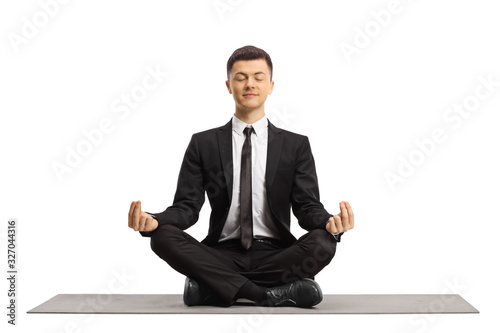 Fototapet Young man in a black suit with closed eyes sitting with crossed legs and making