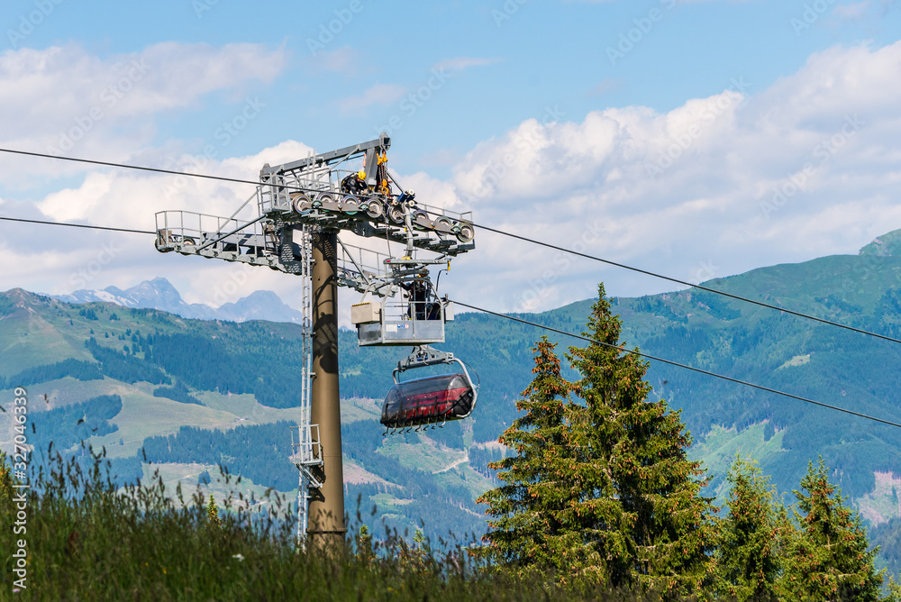 Ski lift technical service during inspection and maintenance of chairlift. Man at work on ski lift tower against the backdrop of mountains and blue, cloudy sky in the summer.